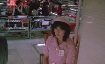 Movie still from “Sans Soleil” (1983), directed by Chris Marker – A woman wearing a pink coat and a hat; Medium shot, Over the shoulder angle