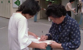 Movie still from “Sans Soleil” (1983), directed by Chris Marker – Two people are writing on a piece of paper; Medium shot, High angle