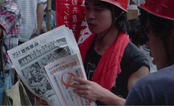 Movie still from “Sans Soleil” (1983), directed by Chris Marker – A woman in a red hat is reading a newspaper; Close Up shot, High angle