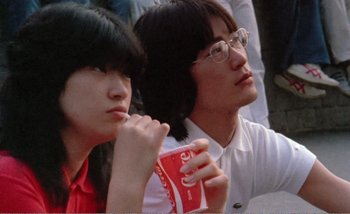 Movie still from “Sans Soleil” (1983), directed by Chris Marker – A man and a woman sitting next to each other holding drinks; Close Up shot, High angle