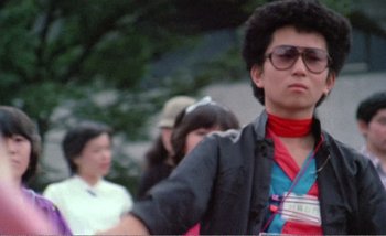 Movie still from “Sans Soleil” (1983), directed by Chris Marker – A young man in a black jacket and a red neck tie; Medium shot, Low angle