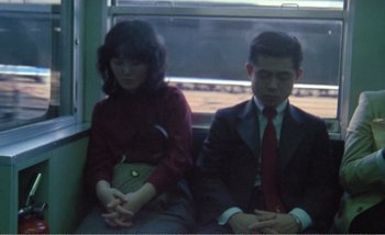 Movie still from “Sans Soleil” (1983), directed by Chris Marker – A man and a woman sitting next to each other on a train; Medium shot, High angle