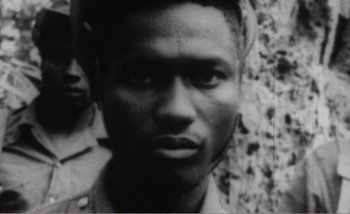 Movie still from “Sans Soleil” (1983), directed by Chris Marker – A black - and - white photo of a man's face in front of a stone wall; Close Up shot, High angle