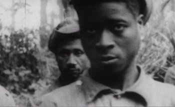 Movie still from “Sans Soleil” (1983), directed by Chris Marker – A black and white photo of two men in the woods; Extreme Close Up shot, High angle