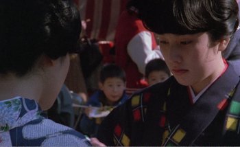 Movie still from “Sans Soleil” (1983), directed by Chris Marker – A group of people sitting in front of each other; Close Up shot, Over the shoulder angle