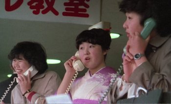 Movie still from “Sans Soleil” (1983), directed by Chris Marker – A woman talking on a phone while sitting next to another woman; Close Up shot, Low angle