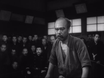 Movie still from “Sanshiro Sugata” (1943), directed by Akira Kurosawa – An old photo of an old man in front of a group of people; Medium shot, Low angle