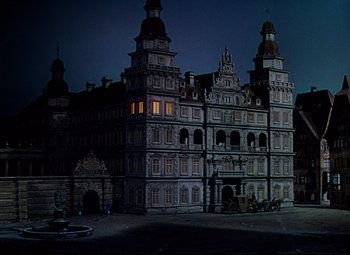 Movie still from “Saraband” (1948), directed by Basil Dearden – A large building that has been lit up at night; Extreme Wide shot, High angle