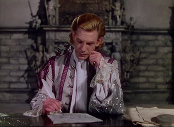 Movie still from “Saraband” (1948), directed by Basil Dearden – A man sitting at a table writing on a piece of paper; Medium shot, High angle