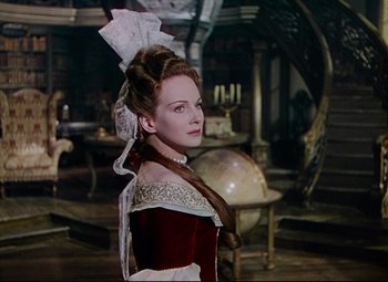 Movie still from “Saraband” (1948), directed by Basil Dearden – A woman in a red and white dress standing next to a globe; Medium shot, Over the shoulder angle