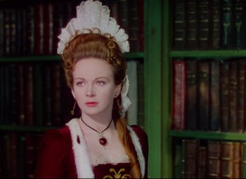 Movie still from “Saraband” (1948), directed by Basil Dearden – A woman in a red and white dress with a book case in the background; Medium shot, Over the shoulder angle