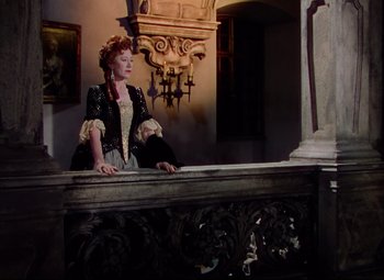Movie still from “Saraband” (1948), directed by Basil Dearden – A woman dressed in period clothing standing next to an ornate bench; Wide shot, Low angle