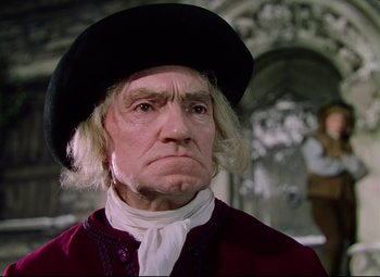 Movie still from “Saraband” (1948), directed by Basil Dearden – An old man wearing a black hat and a red jacket; Close Up shot, Low angle