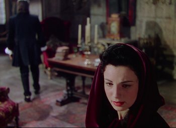 Movie still from “Saraband” (1948), directed by Basil Dearden – A woman with a red head covering in front of a table; Medium shot, Over the shoulder angle