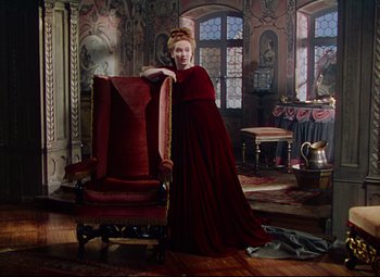 Movie still from “Saraband” (1948), directed by Basil Dearden – A woman in a red dress standing in front of a chair; Wide shot, High angle