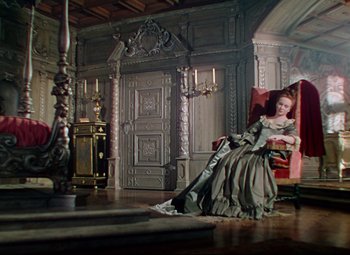 Movie still from “Saraband” (1948), directed by Basil Dearden – A woman sitting in a chair wearing a dress; Wide shot, High angle