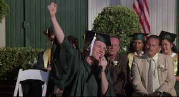 Movie still from “Say Anything” (1989), directed by Cameron Crowe – A woman in a cap and gown singing into a microphone; Medium shot, High angle