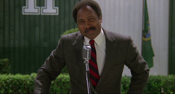Movie still from “Say Anything” (1989), directed by Cameron Crowe – A man in a suit and tie holding a microphone; Medium shot, Low angle
