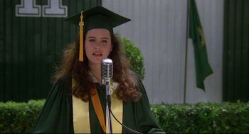 Movie still from “Say Anything” (1989), directed by Cameron Crowe – A woman in a cap and gown standing in front of a microphone; Close Up shot, Low angle