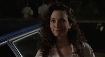 Movie still from “Say Anything” (1989), directed by Cameron Crowe – A woman with long dark curly hair smiles for the camera; Close Up shot, Over the shoulder angle