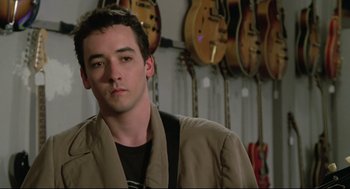 Movie still from “Say Anything” (1989), directed by Cameron Crowe – A man standing in front of a row of guitars; Close Up shot, Over the shoulder angle