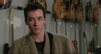 Movie still from “Say Anything” (1989), directed by Cameron Crowe – A man standing in front of a row of guitars; Close Up shot, Over the shoulder angle