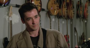 Movie still from “Say Anything” (1989), directed by Cameron Crowe – A young man standing in front of a row of guitars; Close Up shot, Over the shoulder angle