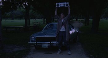 Movie still from “Say Anything” (1989), directed by Cameron Crowe – A man holding a boombox above his head in front of a car; Wide shot, Low angle