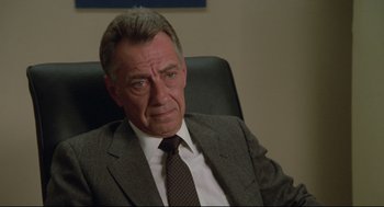 Movie still from “Say Anything” (1989), directed by Cameron Crowe – An older man wearing a suit and tie sitting in an office chair; Close Up shot, Over the shoulder angle