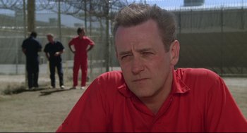 Movie still from “Say Anything” (1989), directed by Cameron Crowe – A man in a red shirt is sitting in front of a fence; Close Up shot, Low angle