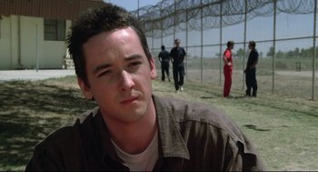 Movie still from “Say Anything” (1989), directed by Cameron Crowe – A young man in a brown shirt is in front of a fence; Close Up shot, Over the shoulder angle