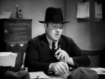 Movie still from “Scarface” (1932), directed by Richard Rosson – A man wearing a hat and a suit is sitting at a table; Close Up shot, High angle