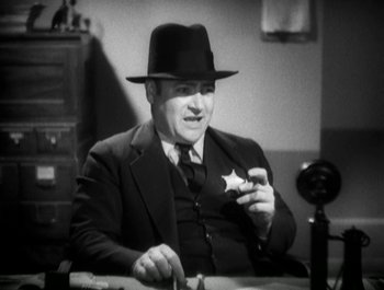 Movie still from “Scarface” (1932), directed by Richard Rosson – An old photo of a man wearing a hat and holding a star; Medium shot, Low angle