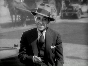 Movie still from “Scarface” (1932), directed by Richard Rosson – A man wearing a suit and a hat smiling for the camera; Medium shot, Low angle