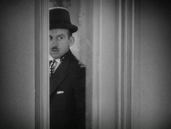 Movie still from “Scarface” (1932), directed by Richard Rosson – A black and white photo of a man in a suit and hat; Medium shot, High angle