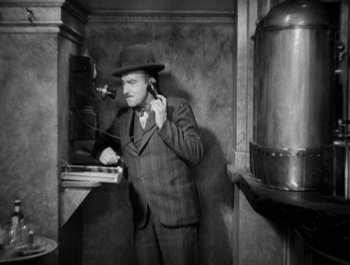 Movie still from “Scarface” (1932), directed by Richard Rosson – A man in a suit and a hat standing next to a stove; Medium shot, High angle