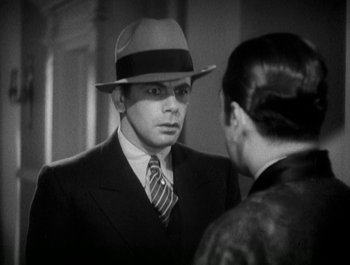 Movie still from “Scarface” (1932), directed by Richard Rosson – A black and white photo of a man in a suit and a hat; Close Up shot, Over the shoulder angle