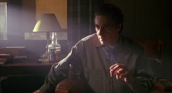 Movie still from “Scent of a Woman” (1992), directed by Martin Brest – A man sitting in a chair in a room with a bottle; Medium shot, Low angle
