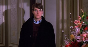 Movie still from “Scent of a Woman” (1992), directed by Martin Brest – A young man in a black coat standing next to a flower bush; Medium shot, Over the shoulder angle