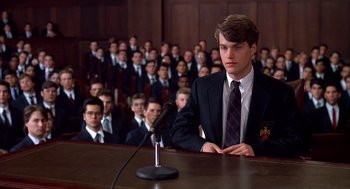 Movie still from “Scent of a Woman” (1992), directed by Martin Brest – A man in a suit and tie sitting at a podium in front of a crowd of people; Medium shot, High angle