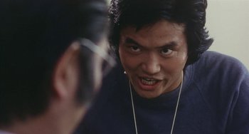 Movie still from “School in the Crosshairs” (1981), directed by Nobuhiko Ôbayashi – A man is looking into a mirror while wearing ear buds; Close Up shot, Over the shoulder angle
