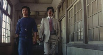 Movie still from “School in the Crosshairs” (1981), directed by Nobuhiko Ôbayashi – A man in a suit walking down a hallway; Medium shot, Low angle
