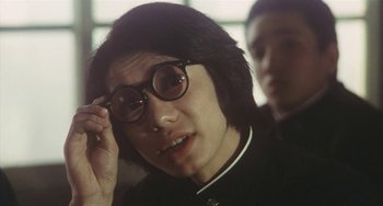 Movie still from “School in the Crosshairs” (1981), directed by Nobuhiko Ôbayashi – A person with glasses is looking at the camera; Close Up shot, Over the shoulder angle