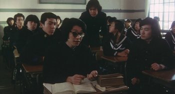 Movie still from “School in the Crosshairs” (1981), directed by Nobuhiko Ôbayashi – A group of people sitting at a table with a book; Medium shot, High angle