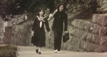 Movie still from “School in the Crosshairs” (1981), directed by Nobuhiko Ôbayashi – A man and a woman walking down a street holding hands; Medium shot, Low angle