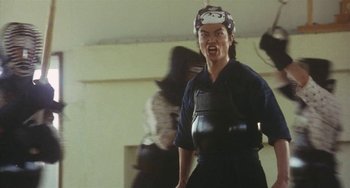 Movie still from “School in the Crosshairs” (1981), directed by Nobuhiko Ôbayashi – A person in a black shirt and a black hat; Medium shot, Low angle