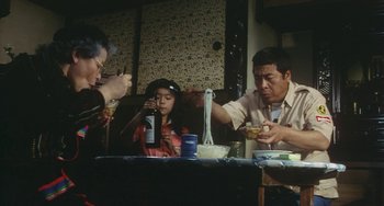 Movie still from “School in the Crosshairs” (1981), directed by Nobuhiko Ôbayashi – Three people sitting at a table eating food; Medium shot, Low angle