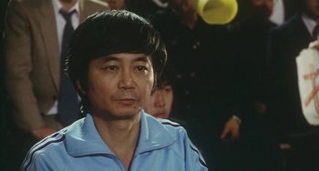 Movie still from “School in the Crosshairs” (1981), directed by Nobuhiko Ôbayashi – An asian man in a blue shirt is looking to his left; Close Up shot, Over the shoulder angle
