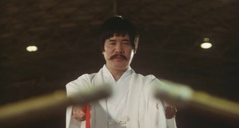 Movie still from “School in the Crosshairs” (1981), directed by Nobuhiko Ôbayashi – A man in a white robe and a red tie; Close Up shot, Low angle