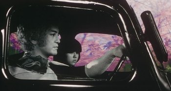Movie still from “School in the Crosshairs” (1981), directed by Nobuhiko Ôbayashi – A man and a woman in a car looking out the window; Medium shot, Low angle